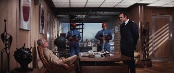 Movie still from “Diamonds Are Forever” (1971), directed by Guy Hamilton – A group of men standing around a table; Wide shot, Low angle