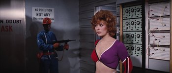 Movie still from “Diamonds Are Forever” (1971), directed by Guy Hamilton – A woman in a purple and red bra holding a gun in front of a man; Medium shot, Over the shoulder angle