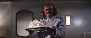 Movie still from “Diamonds Are Forever” (1971), directed by Guy Hamilton – A man holding a cake on top of a silver platter; Medium shot, Over the shoulder angle