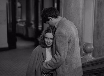 A man and a woman hugging each other in front of a pillar