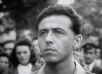 Movie still from “Diary for My Children” (1984), directed by Márta Mészáros – An old black - and - white photo of a man in front of a group of people; Close Up shot, Low angle