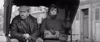 Movie still from “Diary of a Chambermaid” (1964), directed by Luis Buñuel – A black and white photo of a woman holding a purse; Medium shot, Low angle