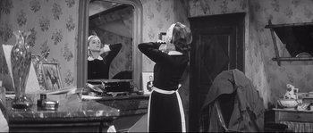 Movie still from “Diary of a Chambermaid” (1964), directed by Luis Buñuel – A black and white photo of a woman in front of a bathroom mirror; Medium shot, Over the shoulder angle
