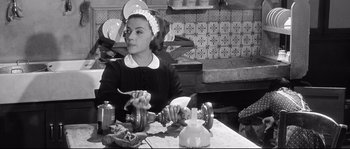 Movie still from “Diary of a Chambermaid” (1964), directed by Luis Buñuel – A woman sitting at a table in front of plates; Medium shot, High angle