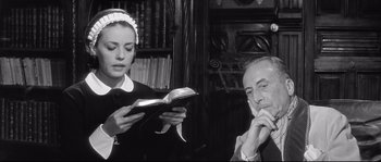 Movie still from “Diary of a Chambermaid” (1964), directed by Luis Buñuel – An old photo of a man and a woman looking at a book; Medium shot, Low angle