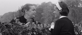 Movie still from “Diary of a Chambermaid” (1964), directed by Luis Buñuel – Two women talking to each other in front of a fence; Medium shot, Over the shoulder angle