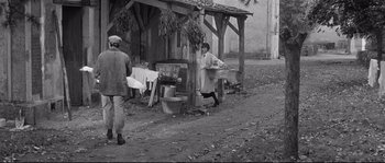 Movie still from “Diary of a Chambermaid” (1964), directed by Luis Buñuel – An old photo of a man and a woman in front of an outdoor market; Wide shot, High angle