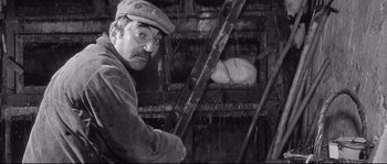Movie still from “Diary of a Chambermaid” (1964), directed by Luis Buñuel – A man in a hat sitting next to a ladder; Medium shot, High angle