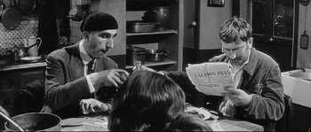 Movie still from “Diary of a Chambermaid” (1964), directed by Luis Buñuel – A group of people sitting at a table with a newspaper; Medium shot, Over the shoulder angle