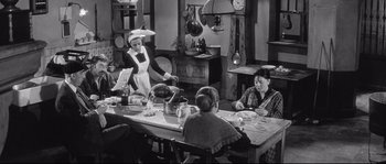 Movie still from “Diary of a Chambermaid” (1964), directed by Luis Buñuel – An old photo of three people sitting at a dinner table; Wide shot, High angle