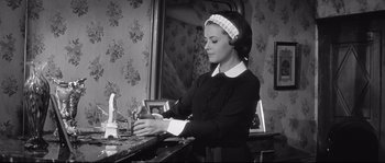 Movie still from “Diary of a Chambermaid” (1964), directed by Luis Buñuel – A black and white photo of a woman in a kitchen; Medium shot, Low angle
