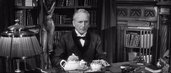 Movie still from “Diary of a Chambermaid” (1964), directed by Luis Buñuel – An older man sitting at a table with a tea pot; Medium shot, Low angle