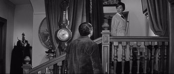Movie still from “Diary of a Chambermaid” (1964), directed by Luis Buñuel – A man standing in front of a woman in front of a clock; Medium shot, High angle
