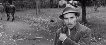 Movie still from “Diary of a Chambermaid” (1964), directed by Luis Buñuel – A man in a hat and a jacket standing in a field; Close Up shot, Over the shoulder angle