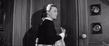 Movie still from “Diary of a Chambermaid” (1964), directed by Luis Buñuel – A black and white photo of a woman in a maid's outfit; Medium shot, Low angle