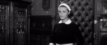 Movie still from “Diary of a Chambermaid” (1964), directed by Luis Buñuel – A woman in a maid's outfit standing in front of a fireplace; Medium shot, Low angle