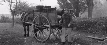 Movie still from “Diary of a Chambermaid” (1964), directed by Luis Buñuel – A man standing in front of an old wagon; Wide shot, Low angle