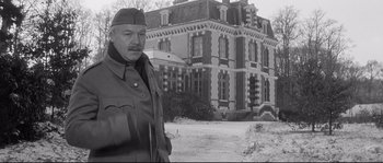 Movie still from “Diary of a Chambermaid” (1964), directed by Luis Buñuel – An older man standing in front of an old building; Medium shot, Low angle