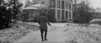 Movie still from “Diary of a Chambermaid” (1964), directed by Luis Buñuel – A man walking down a snowy path in front of a building; Wide shot, Low angle