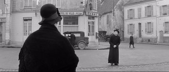 Movie still from “Diary of a Chambermaid” (1964), directed by Luis Buñuel – A woman in a long black dress standing in front of an old car; Wide shot, Over the shoulder angle