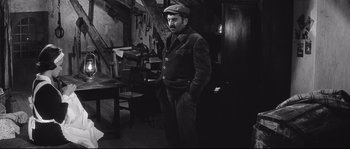 Movie still from “Diary of a Chambermaid” (1964), directed by Luis Buñuel – A man standing in front of a wooden table and chair; Medium shot, High angle
