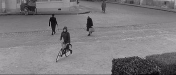 Movie still from “Diary of a Chambermaid” (1964), directed by Luis Buñuel – An old black and white photo of a woman riding a bike; Extreme Wide shot, High angle