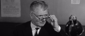 Movie still from “Diary of a Chambermaid” (1964), directed by Luis Buñuel – An older man in a suit and tie holding a pair of eyeglasses; Close Up shot, Over the shoulder angle