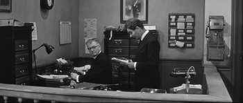 Movie still from “Diary of a Chambermaid” (1964), directed by Luis Buñuel – Two men in suits are sitting at a desk; Medium shot, Low angle