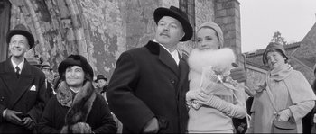 Movie still from “Diary of a Chambermaid” (1964), directed by Luis Buñuel – A man and a woman standing next to each other in front of a brick wall; Medium shot, Low angle