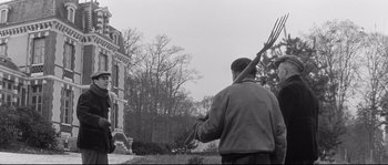 Movie still from “Diary of a Chambermaid” (1964), directed by Luis Buñuel – A man holding a bunch of sticks in his hand; Wide shot, Low angle