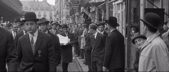 Movie still from “Diary of a Chambermaid” (1964), directed by Luis Buñuel – A group of men standing on the side of a street; Wide shot, High angle