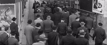 Movie still from “Diary of a Chambermaid” (1964), directed by Luis Buñuel – A group of men in suits and hats walking down a street; Wide shot, High angle