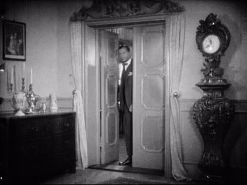 Movie still from “Diary of a Lost Girl” (1929), directed by Georg Wilhelm Pabst – A black and white photo of a man standing in a doorway; Wide shot, High angle