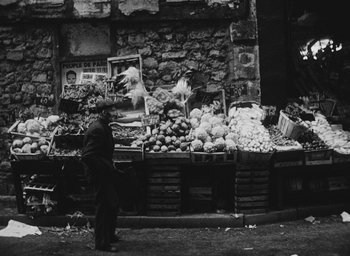 Movie still from “Diary of a Pregnant Woman” (1958), directed by Agnès Varda – A man standing in front of a fruit stand; Wide shot, Over the shoulder angle
