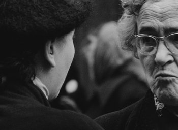Movie still from “Diary of a Pregnant Woman” (1958), directed by Agnès Varda – A woman wearing a hat and glasses talking to another woman; Close Up shot, Over the shoulder angle