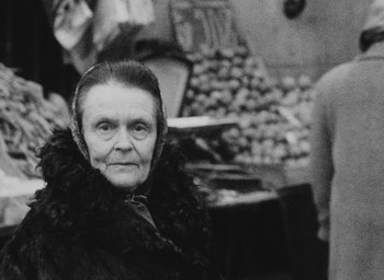 Movie still from “Diary of a Pregnant Woman” (1958), directed by Agnès Varda – An old woman wearing a fur coat in front of a fruit stand; Close Up shot, Over the shoulder angle