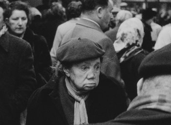 Movie still from “Diary of a Pregnant Woman” (1958), directed by Agnès Varda – An older woman wearing a hat and a scarf; Close Up shot, High angle
