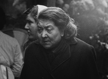 Movie still from “Diary of a Pregnant Woman” (1958), directed by Agnès Varda – An older woman wearing a black coat and a white hat; Close Up shot, Over the shoulder angle