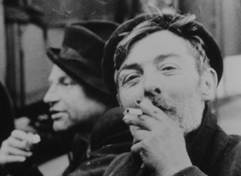 Movie still from “Diary of a Pregnant Woman” (1958), directed by Agnès Varda – A man smoking a cigarette while sitting next to another man; Close Up shot, Over the shoulder angle