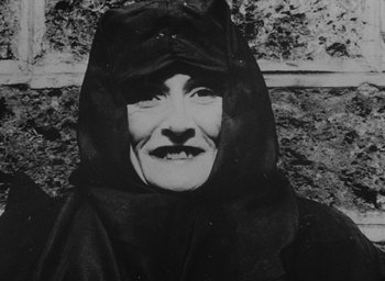 Movie still from “Diary of a Pregnant Woman” (1958), directed by Agnès Varda – An old woman wearing a black robe and a hood; Close Up shot, High angle