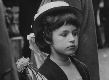 Movie still from “Diary of a Pregnant Woman” (1958), directed by Agnès Varda – A little girl wearing a hat and holding a flower; Close Up shot, Over the shoulder angle