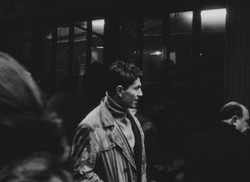 Movie still from “Diary of a Pregnant Woman” (1958), directed by Agnès Varda – A black and white photo of a man in a trench coat; Close Up shot, Over the shoulder angle