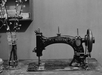 Movie still from “Diary of a Pregnant Woman” (1958), directed by Agnès Varda – An old fashioned sewing machine sitting in a room; Medium shot, Low angle
