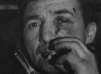 Movie still from “Diary of a Pregnant Woman” (1958), directed by Agnès Varda – A black and white photo of a man smoking a cigarette; Close Up shot, High angle