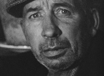 Movie still from “Diary of a Pregnant Woman” (1958), directed by Agnès Varda – Black and white photograph of a man wearing a hat; Extreme Close Up shot, High angle