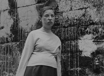 Movie still from “Diary of a Pregnant Woman” (1958), directed by Agnès Varda – A black and white photo of a woman standing in front of a wall; Medium shot, Low angle