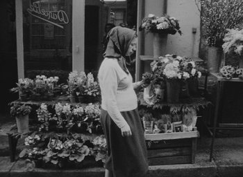 Movie still from “Diary of a Pregnant Woman” (1958), directed by Agnès Varda – A woman wearing a headscarf is looking at flowers; Wide shot, High angle