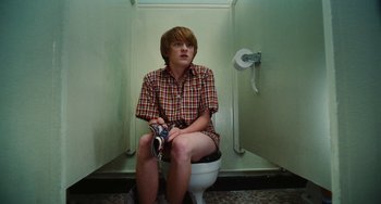 Movie still from “Diary of a Wimpy Kid” (2010), directed by Thor Freudenthal – A man sitting on top of a toilet holding a beer; Medium shot, High angle