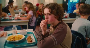 Movie still from “Diary of a Wimpy Kid” (2010), directed by Thor Freudenthal – A young man eating a hot dog at a table; Medium shot, Over the shoulder angle