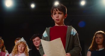 Movie still from “Diary of a Wimpy Kid” (2010), directed by Thor Freudenthal – A young boy holding a piece of paper in front of a group of people; Medium shot, Over the shoulder angle